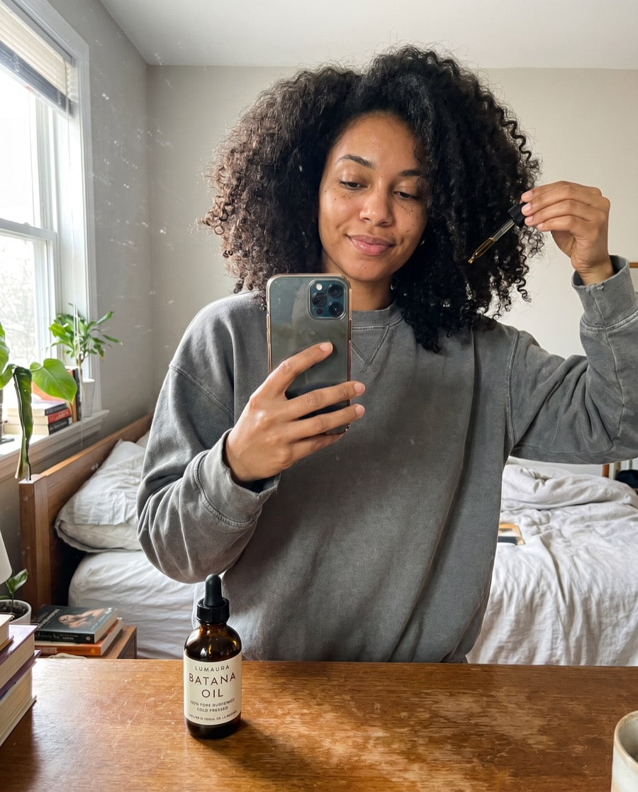 Bottle of Lumaura batana oil held up in front of a mirror